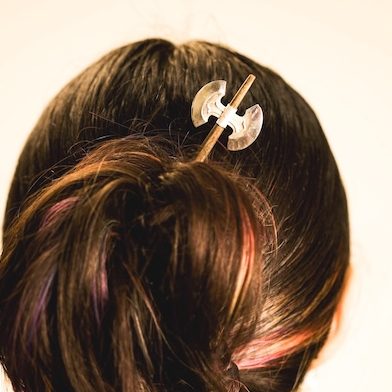 Back of woman's head showing a hairpin that looks like a tiny battle axe.