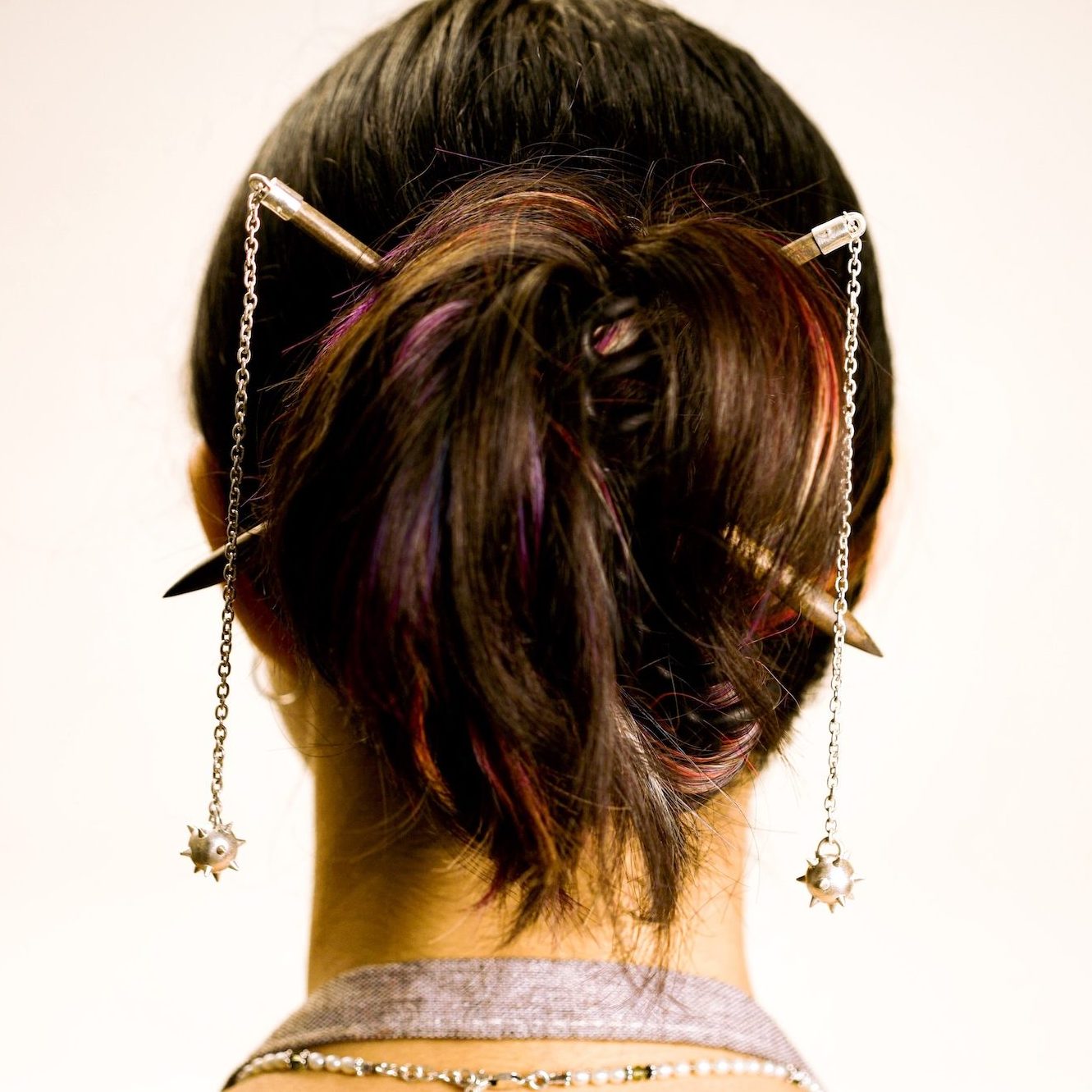 Back of woman's head showing hairpins that looks flails, ie medieval weapons.